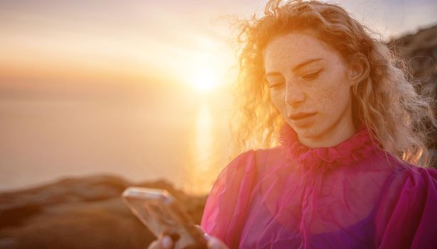 Side view a Young beautiful sensual woman in a red long dress posing on a volcanic rock high above the sea during sunset. Girl on the nature on overcast sky background. Fashion photo