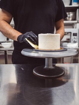 Decorator using spatula and scraper to smooth buttercream on a frosted cake