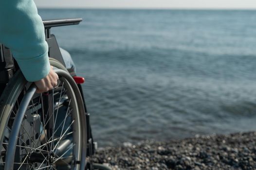 Caucasian woman in a wheelchair on the seashore. Close-up of female hands