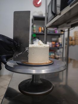 Decorator using spatula and scraper to smooth buttercream on a frosted cake