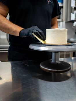 Decorator using spatula and scraper to smooth buttercream on a frosted cake