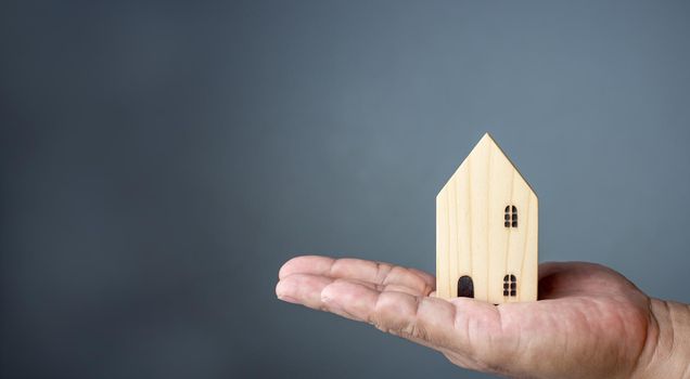 Concept of selling a house. A hand is holding a model house on a gray background. Real estate agent offer house, property insurance and security, affordable housing concepts, home insurance broker agent, salesman person.