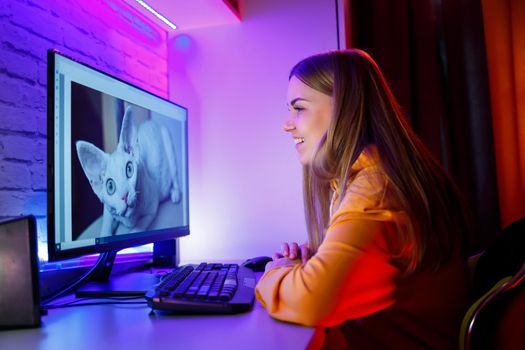 Girl freelancer looks on a computer screen at a cat. Sitting in an apartment at a computer desk