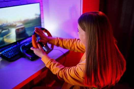 girl gamer playing racing on a computer. She uses a steering wheel. emotional play