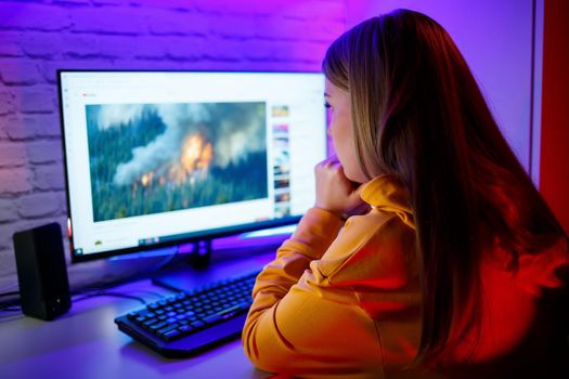 girl freelancer looks on the computer screen news about forest fires and the virus COVID-19