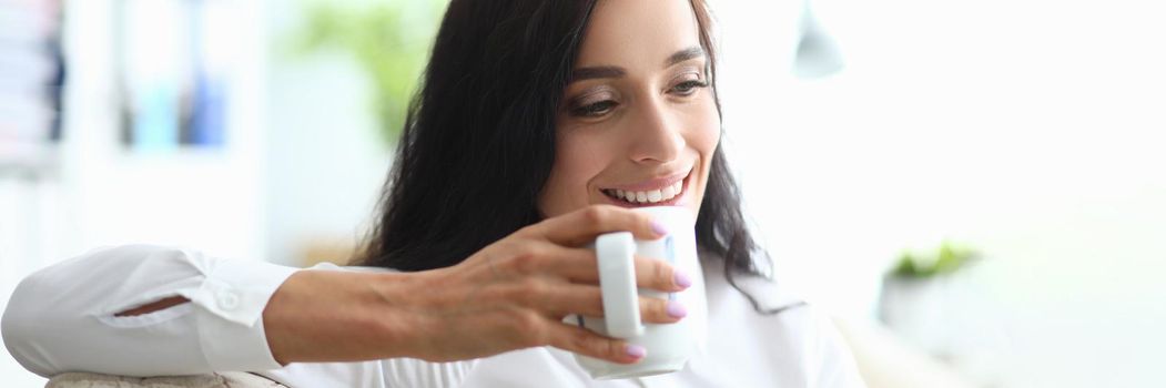 Young woman drinks from cup while sitting on couch. Drinking regimen of day concept