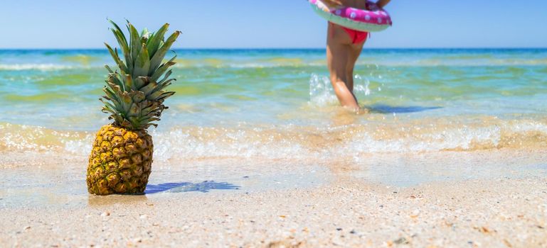 Pineapple on beach and kid running in the water background. Tropical background. Summer holiday concept. High quality photo