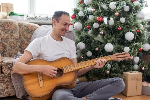 young handsome man sitting on the sofa, he is playing guitar, music, christmas, relax concept.