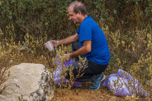 man with garbage bags and gloves cleaning the bush from polluting debris