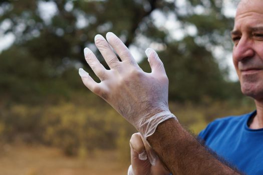 man putting on white latex gloves in the field to clean up, with trees in the background