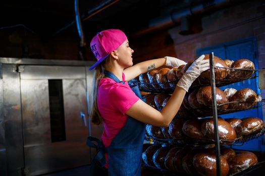 A young girl works in a bakery. She puts bread on a shelf. Woman baker at workplace in a bakery. A professional baker holds bread in his hands. Bread production concept