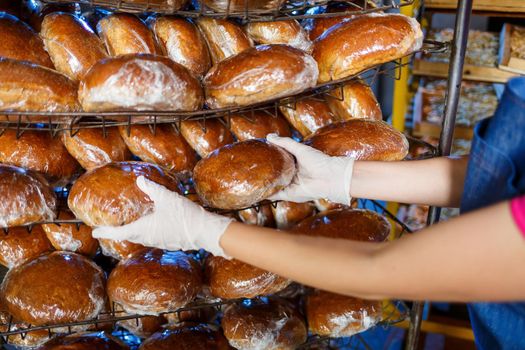 A worker works in a bakery. She puts bread on a shelf. Fresh crispy bread close-up