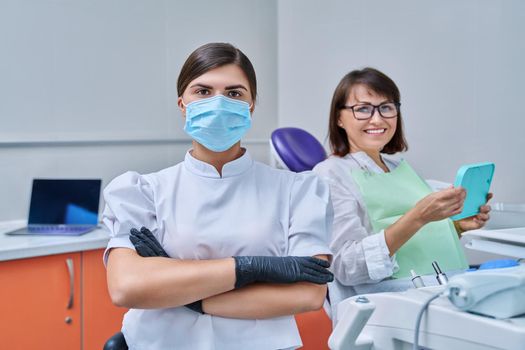 Portrait of young female doctor dentist looking at camera with mature woman patient sitting in dental chair. Dentistry, hygiene, treatment, medicine, dental health care concept