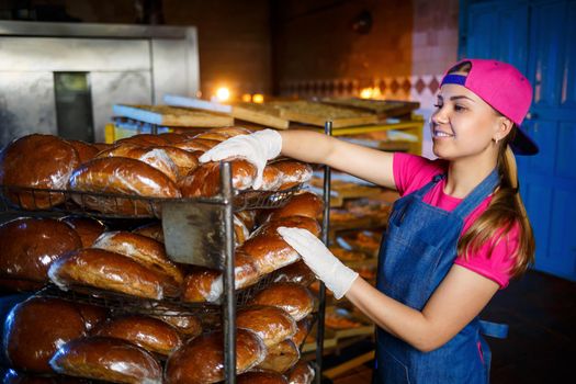 Professional baker - a young pretty woman in a denim apron holds fresh bread in her hands. Bakery products. Bread production