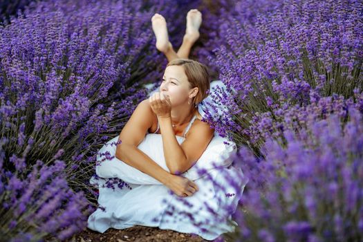 A middle-aged woman lies in a lavender field and enjoys aromatherapy. Aromatherapy concept, lavender oil, photo session in lavender.