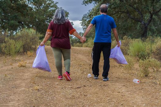 couple of environmentalists with garbage bags walking hand in hand along a road full of garbage