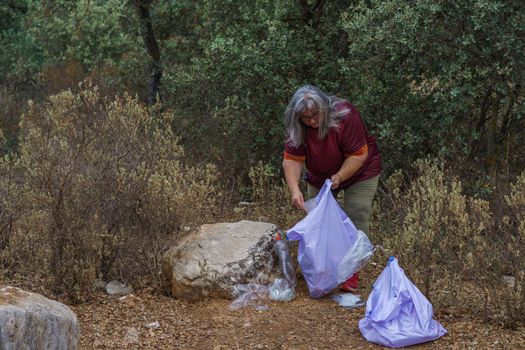 adult white-haired female environmentalist with garbage bags picking up trash from the field