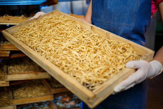 The girl works on the production of spaghetti. Making noodles. Pasta factory. Stage production of pasta. Raw noodles. Worker with a box of pasta.