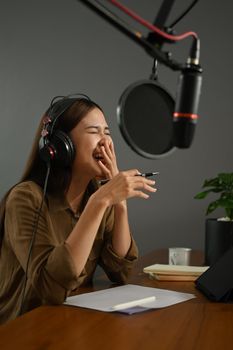Cheerful young female radio host laughing while interviewing guest and recording live podcast in home studio.