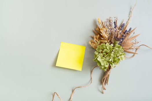 Blank colored paper for notes and a bouquet of dry flowers and herbs on a colored background.