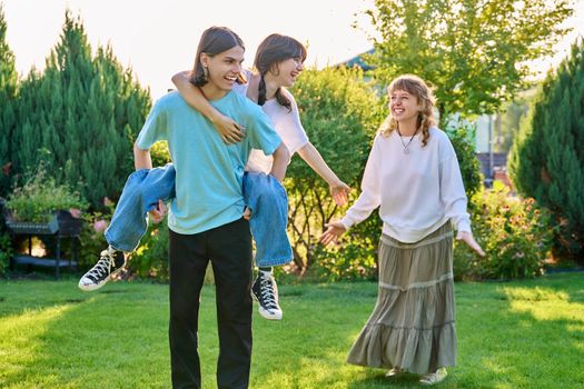 Three teenage friends having fun outdoor, sunny summer day on the lawn. Group of teenagers laughing together. Lifestyle, leisure, friendship, youth concept