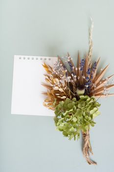 Blank paper for notes and a bouquet of dry flowers and herbs on a colored background.