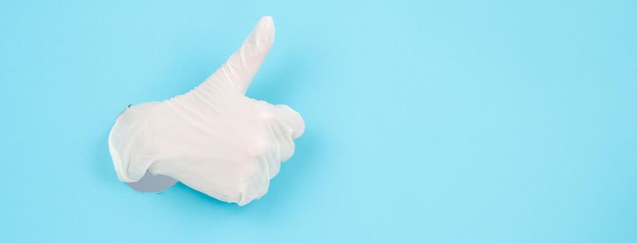 A female gloved hand sticks out through a blue paper background and shows a thumbs up. Widescreen