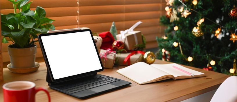 Digital tablet with blank screen and Christmas gift boxes on wooden table.