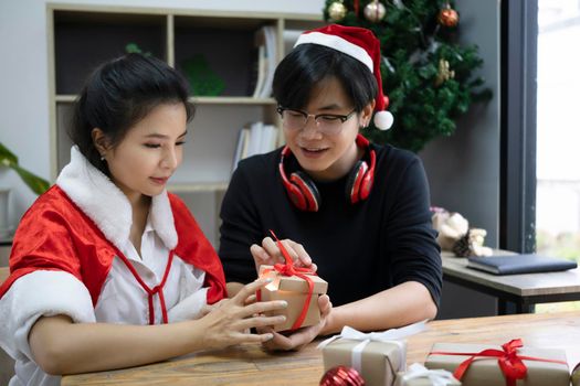 Young asian couple opening Christmas gift box together living room.