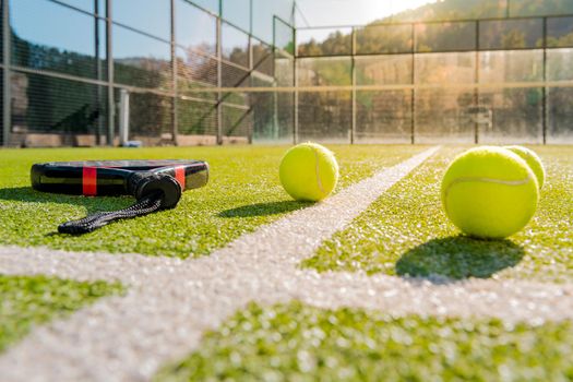 outdoors paddle tennis court with racket and yellow balls on the artificial turf at sunset, indoor sports concept and sporty lifestyle
