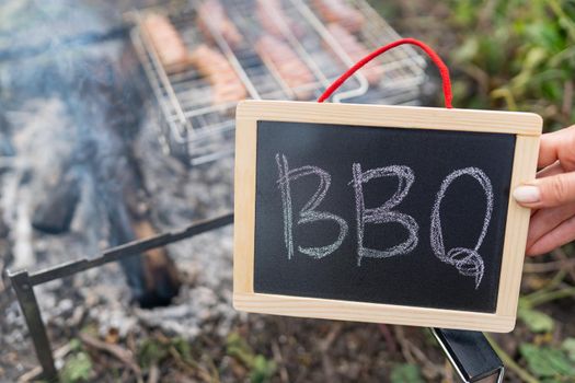 The inscription barbecue on a black plate, a fire against the background of a grill grate on which sausages lie