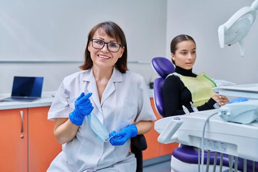 Portrait of female dentist looking at camera with young teen girl patient sitting in dental chair. Dentistry, hygiene, treatment, dental health care concept