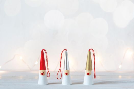 three Santa Clauses figurines on a white background, garland lights, side view, copy space