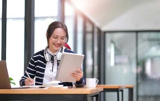 Young adult happy smiling Hispanic Asian student wearing headphones talking on online chat meeting using laptop in university campus or at virtual office. College female student learning remotely..