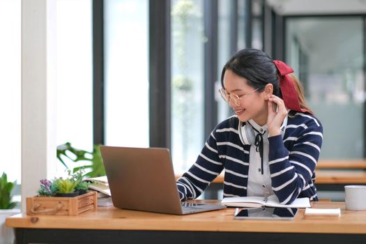 Student learning on laptop indoors- educational course or training, seminar, education online concept, Asian woman with modern laptop and headphones learning at home.