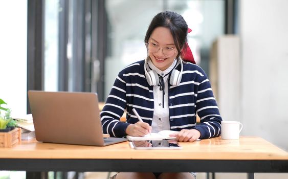 Student learning on laptop indoors- educational course or training, seminar, education online concept, Asian woman with modern laptop and headphones learning at home.