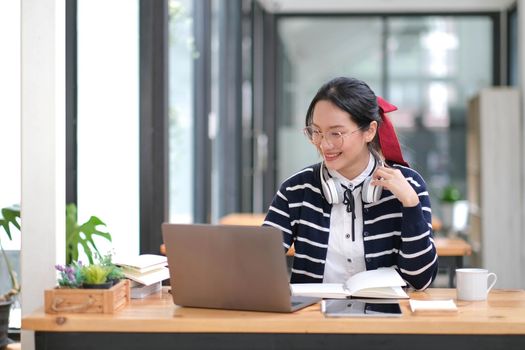 Student learning on laptop indoors- educational course or training, seminar, education online concept, Asian woman with modern laptop and headphones learning at home.