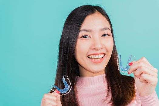 Portrait Asian beautiful young woman smiling hold silicone orthodontic retainers for teeth, Teeth retaining tools after removable braces, isolated blue background, Dental hygiene healthy care concept