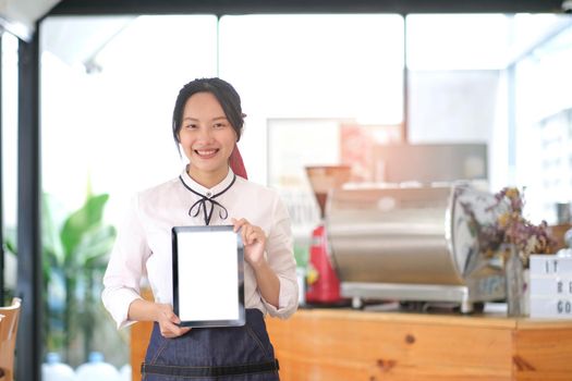 portrait of a woman wearing an apron holding a digital tablet with a blank white screen. Waiter holding a touch screen tab with copy space