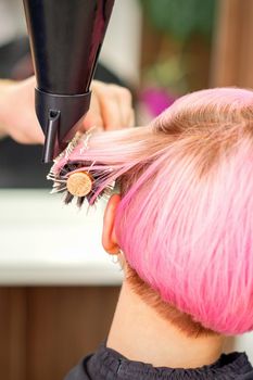 A professional hairdresser is drying long red hair with a hair dryer and round brush, close up