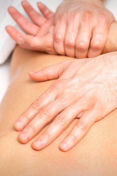 A male physiotherapist stretches the arms on the back of a man lying down, close up