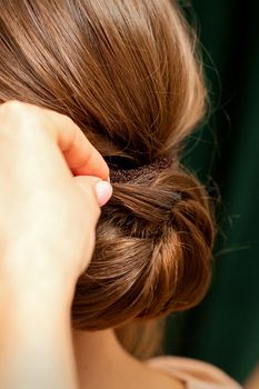 Hands of hairdresser making french twist hairstyle of an unrecognizable young brunette woman in a beauty salon, back view, close up