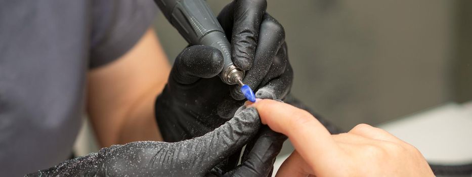 Manicurist removes nail polish uses the electric machine of the nail file during manicure in a nail salon