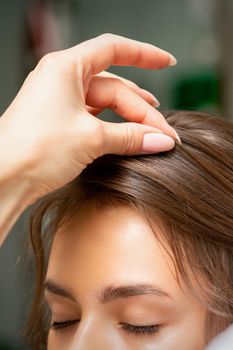 A hairdresser is making the hairstyle of a young brunette woman in a hair salon, close up