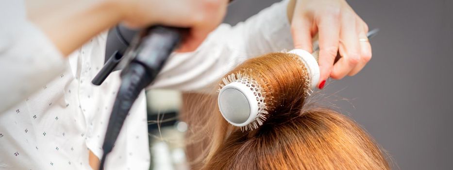 Drying red hair with a hairdryer and round brush, close up