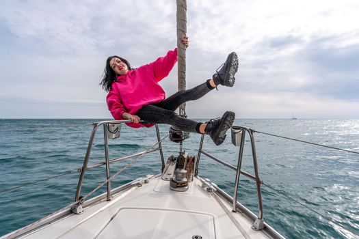 Woman standing on the nose of the yacht at a sunny summer day, breeze developing hair, beautiful sea on background.