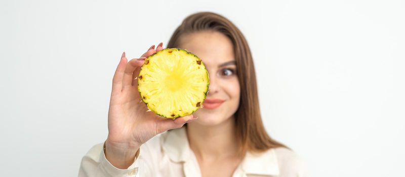 A young attractive pretty nice caucasian smiling woman holds ring slice pineapple covering her eye against a white background. Healthy eating concept