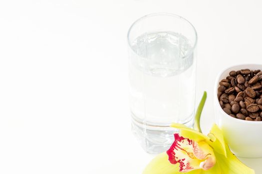 Cup of coffee beans and glass of water with yellow orchid flower against a white background