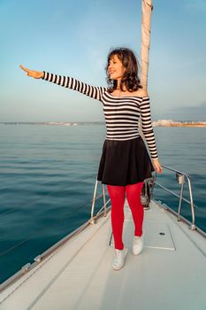 Woman standing on the nose of the yacht at a sunny summer day, breeze developing hair, beautiful sea on background.