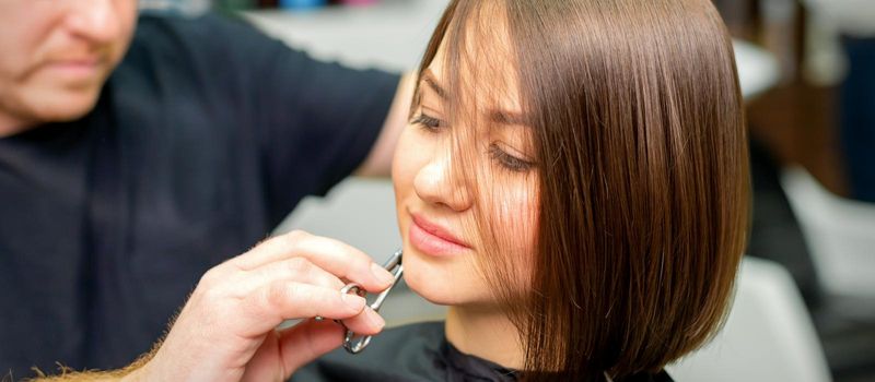 The hairdresser cuts the hair of a brunette woman. Hairstylist is cutting the hair of female client in a professional hair salon, close up